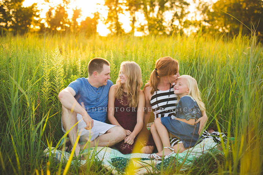 Parents and four children sitting on a picnic blanket in the sunset.